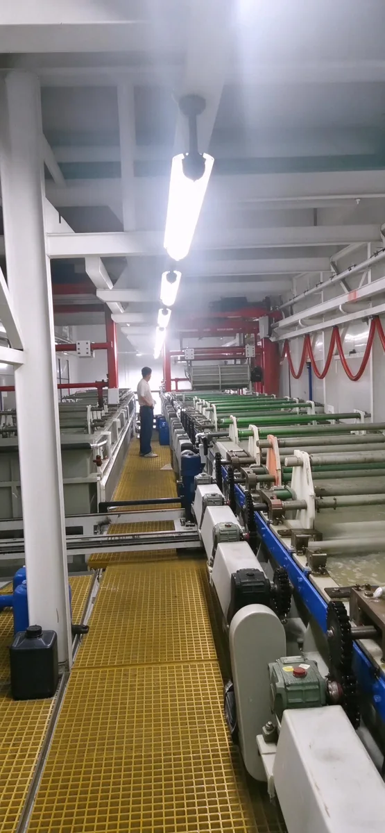 Industrial automated barrel plating production line with green rollers and yellow walkway